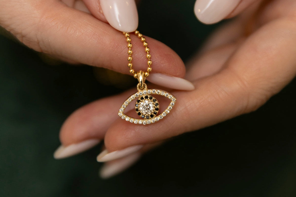 Gold necklace with an eye-shaped pendant held by a hand against a dark background