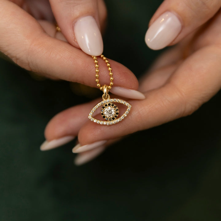 Gold necklace with an eye-shaped pendant held by a hand against a dark background